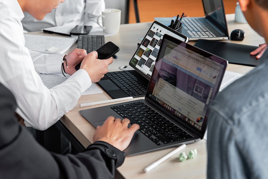 Professionals in a modern office discussing work with laptops and smartphones.